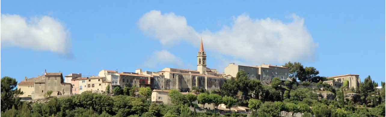Village médiéval La Cadière d'Azur perché avec un clocher sous un ciel bleu et des arbres verdoyants.